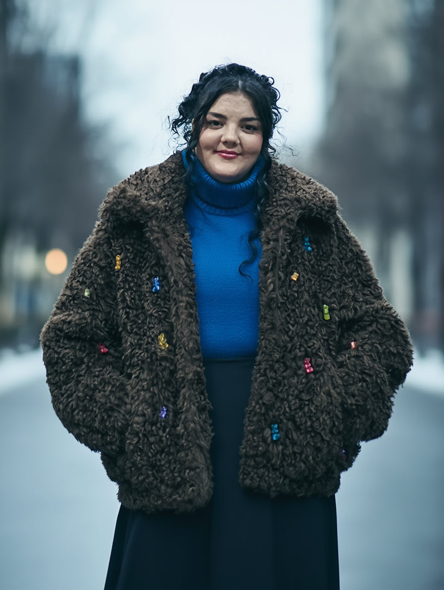 chica veintitantos con abrigo franela marrón oversize con ositos tipo gominola cosidos. Jersey cuello alto y falda larga